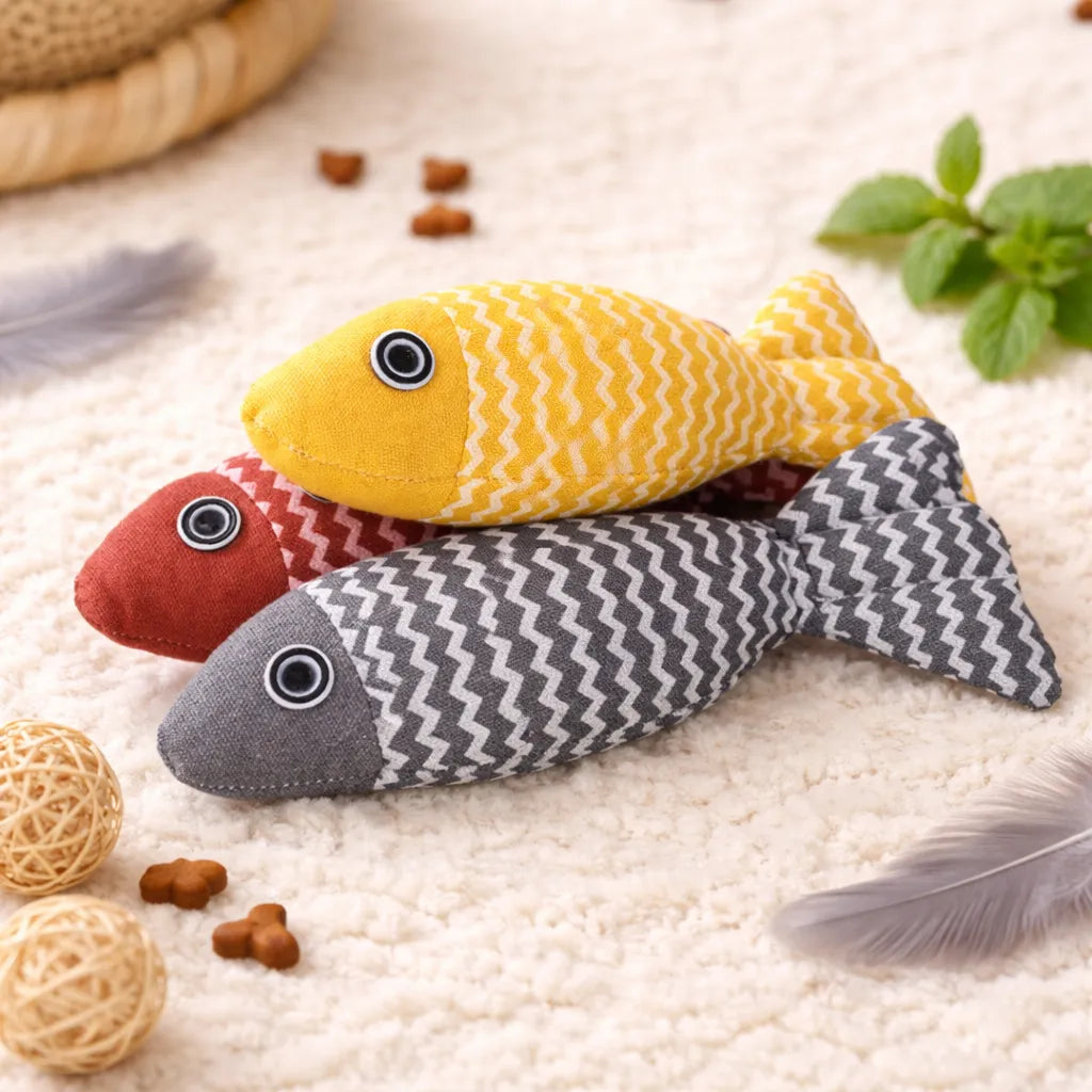 Three soft fabric fish catnip toys in yellow, red, and gray with zigzag patterns on a cream rug.