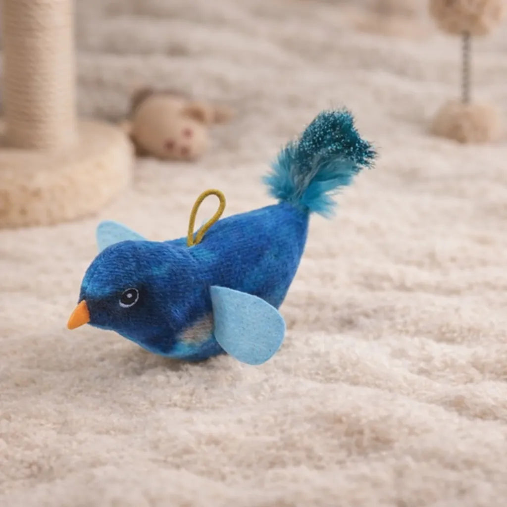 Blue plush chirping bird cat toy with an orange beak, light blue wings, and a fluffy blue tail on a beige rug.