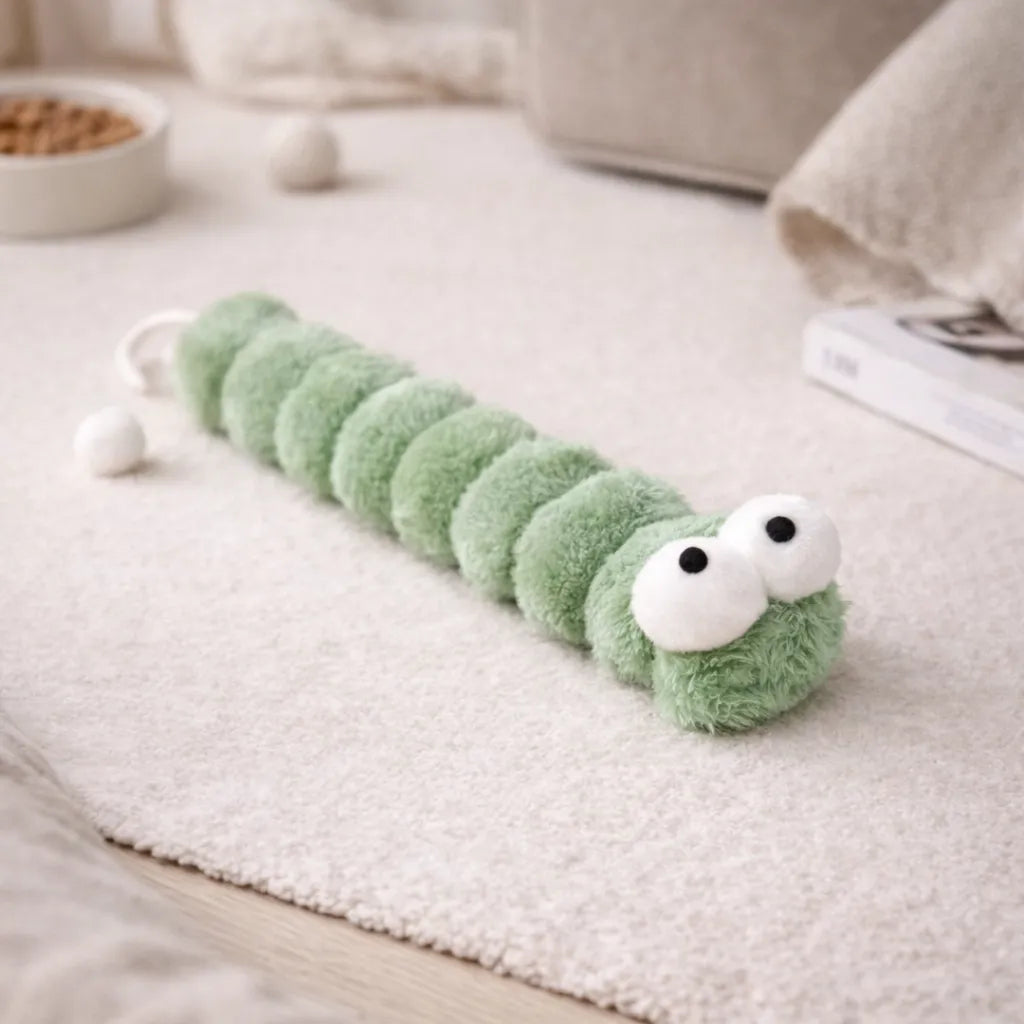 Green plush caterpillar catnip kicker toy with large white eyes on a light rug.