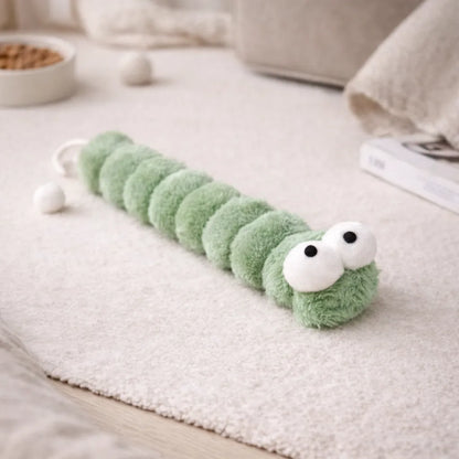 Green plush caterpillar catnip kicker toy with large white eyes on a light rug.