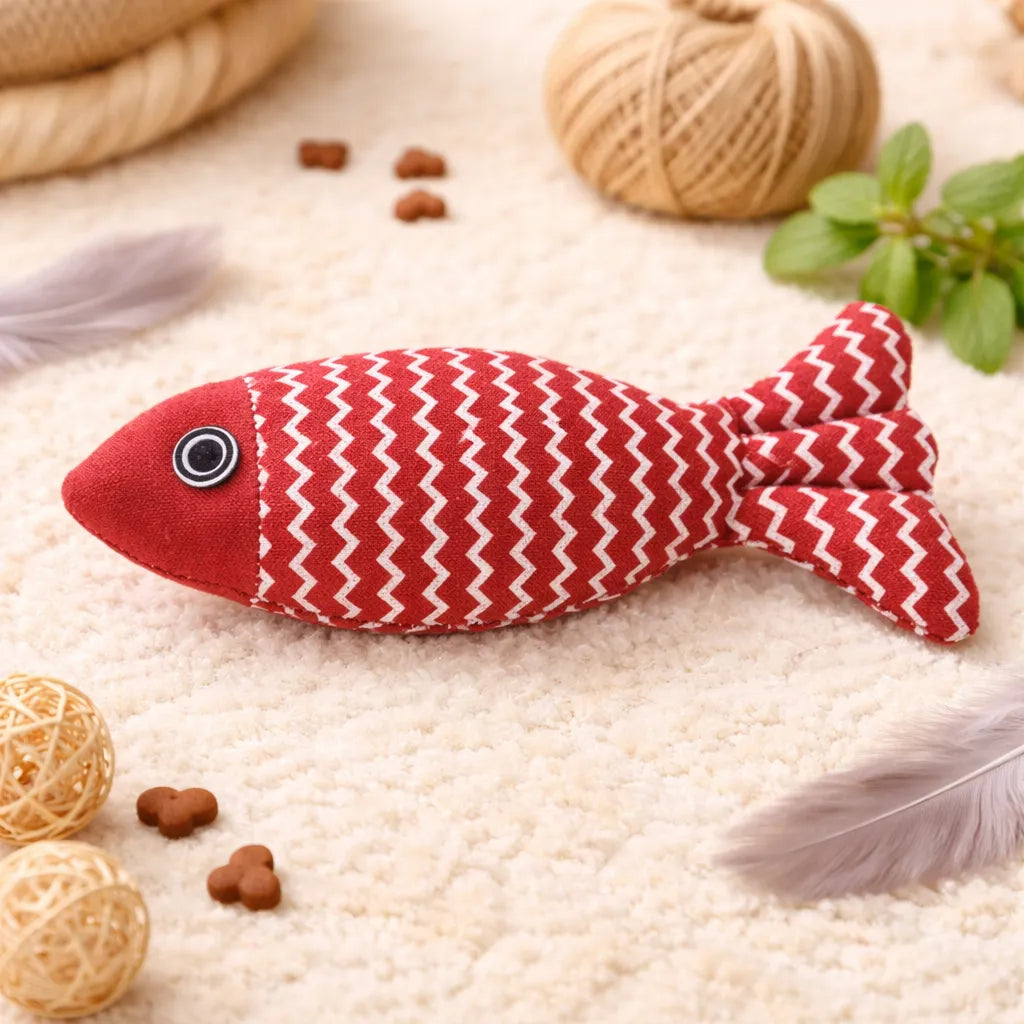 Red fabric fish catnip toy with white zigzag pattern, black eye, on a cream rug.