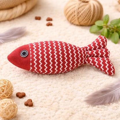 Red fabric fish catnip toy with white zigzag pattern, black eye, on a cream rug.