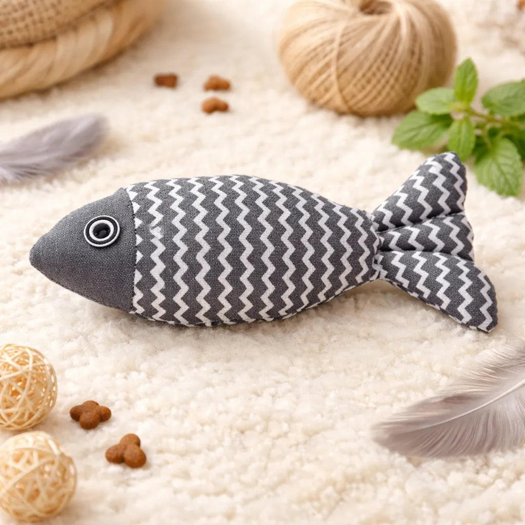 Gray fabric fish catnip toy with white zigzag pattern, black eye, on a cream rug.