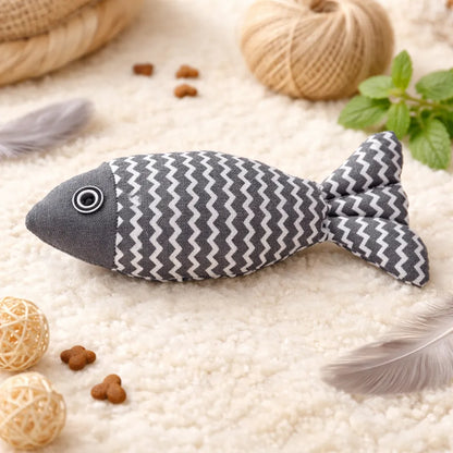 Gray fabric fish catnip toy with white zigzag pattern, black eye, on a cream rug.