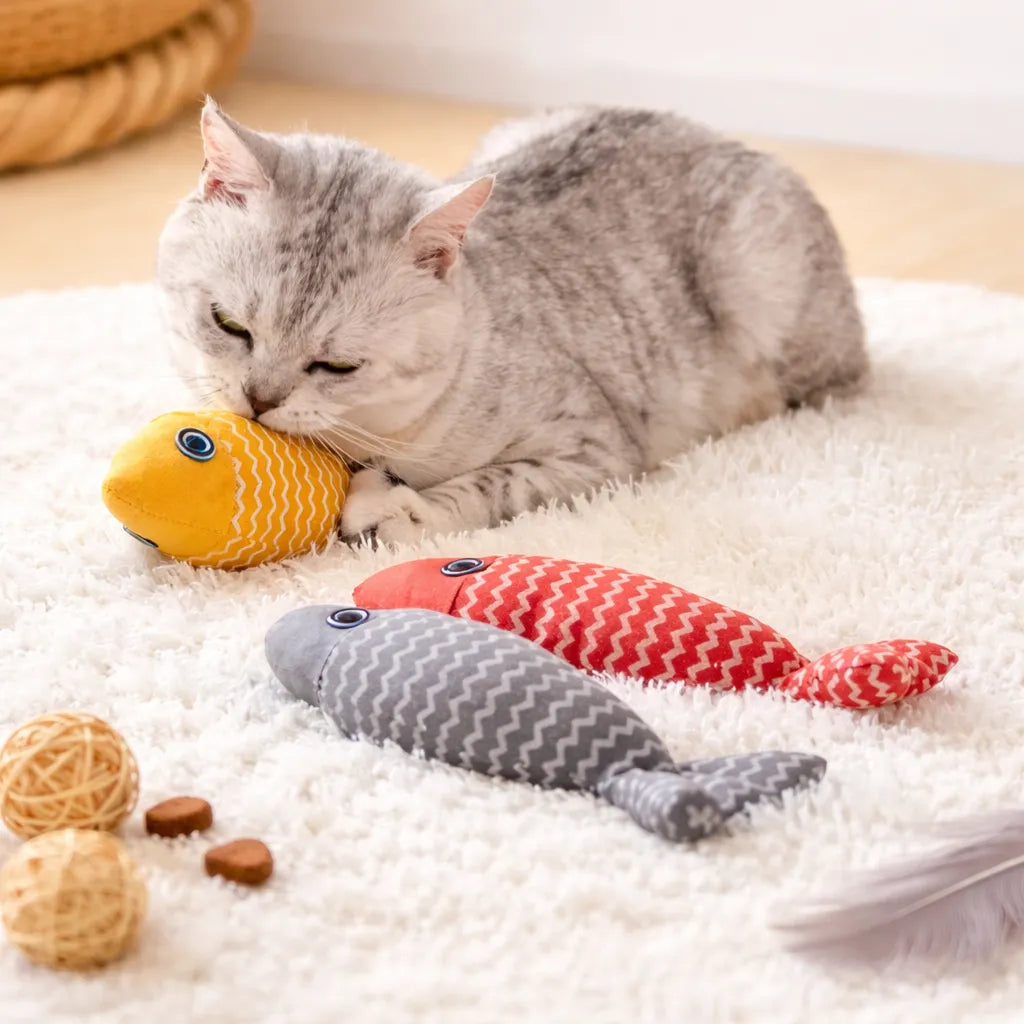 Silver cat cuddling a yellow fish catnip toy, with red and grey fish toys on a white rug.