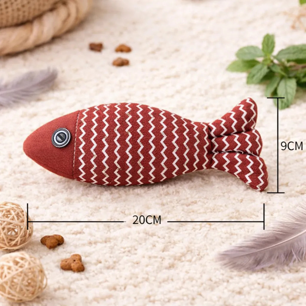 Red fabric fish catnip toy with white zigzags, black button eye, 20cm long, on a cream rug.