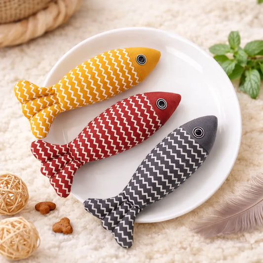 Three soft fabric fish catnip toys in yellow, red, and grey with white zigzag patterns on a white plate.