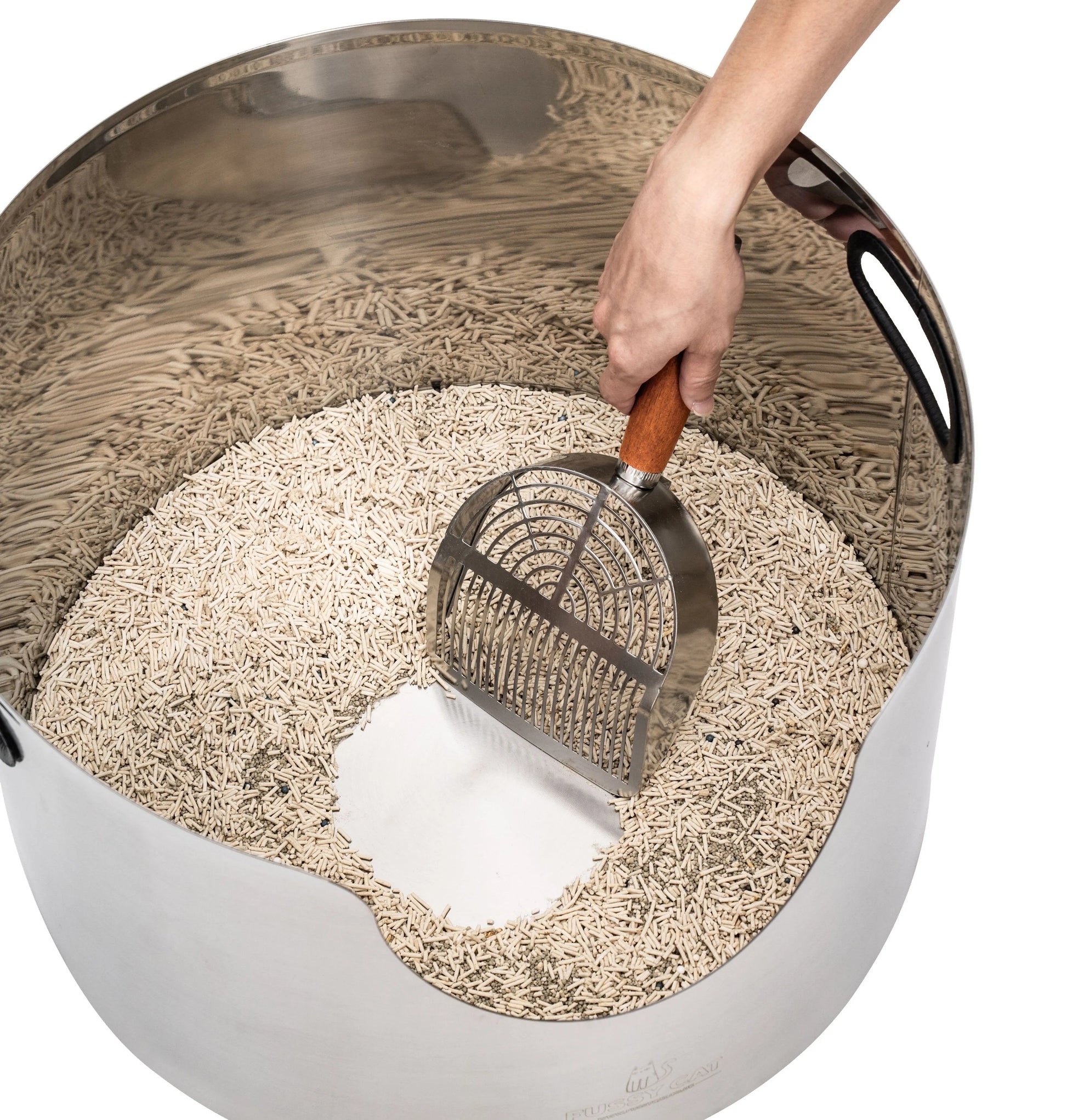 Hand scooping a round, premium stainless steel litter box filled with natural cat litter.