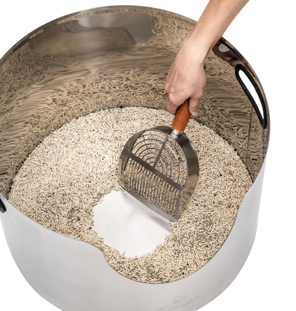 Hand scooping a round, premium stainless steel litter box filled with natural cat litter.