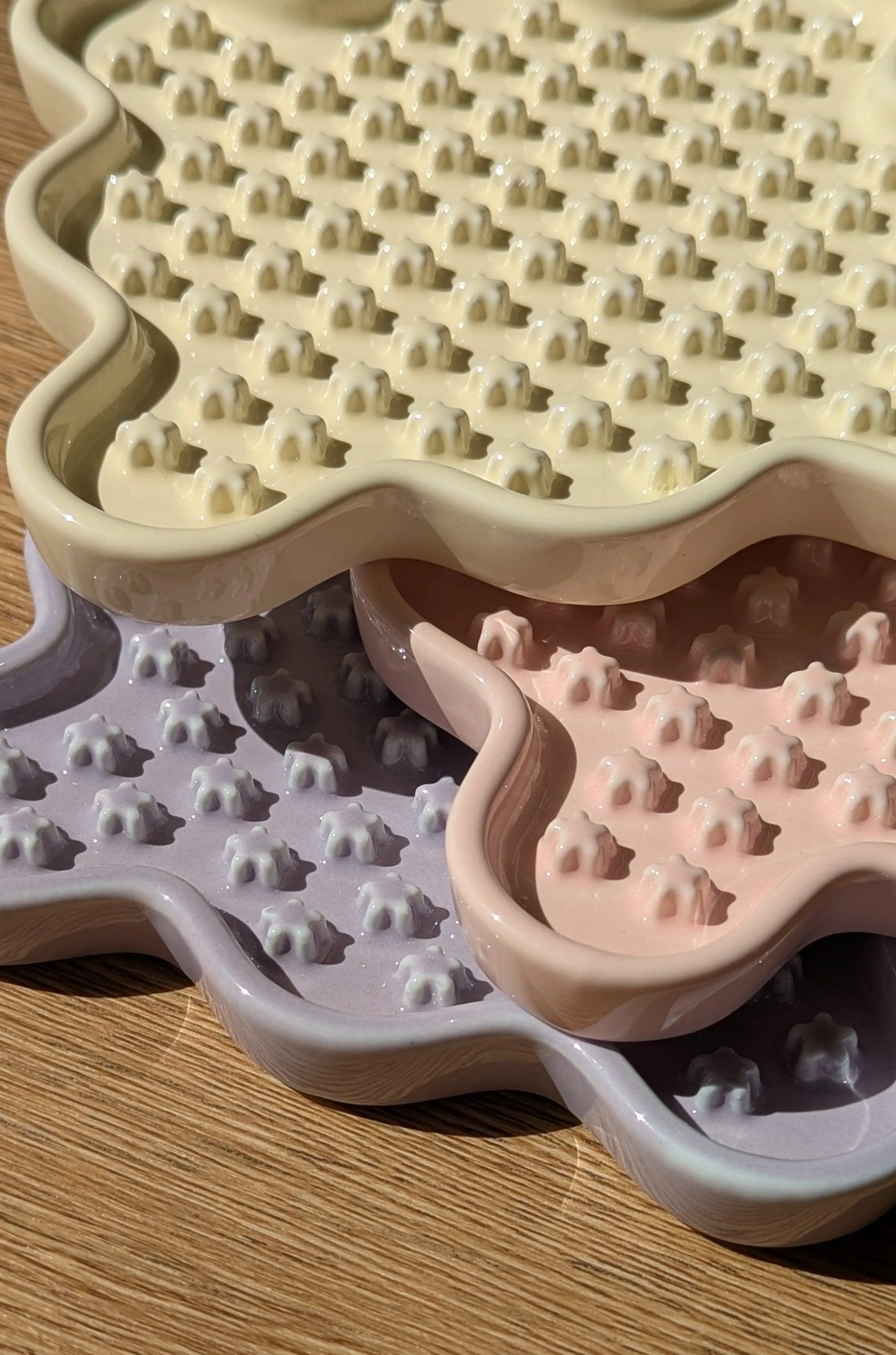 Three pastel ceramic Fussy Cat slow feeders in cream, pink, and lavender with flower-shaped nubs.