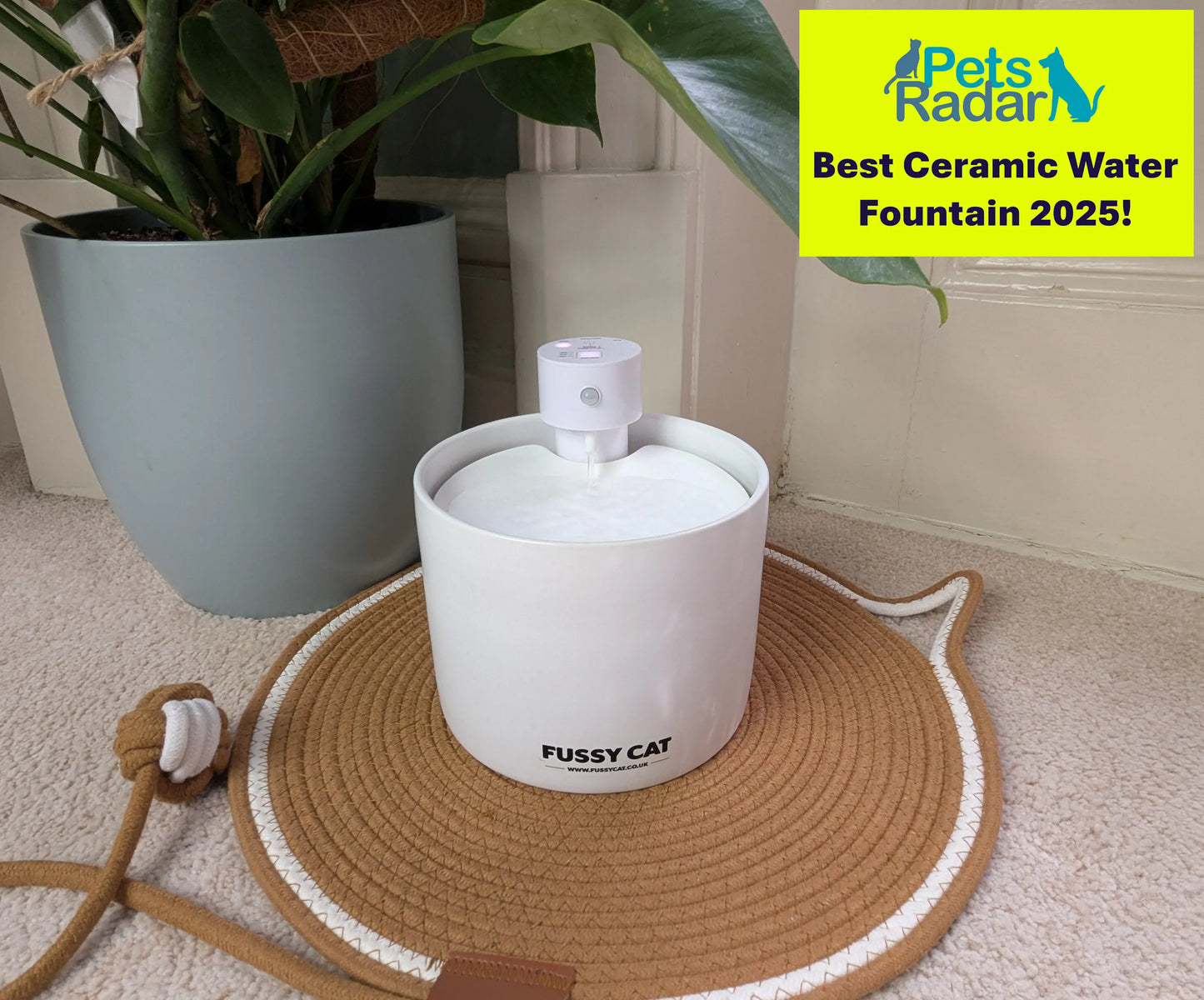 White ceramic Fussy Cat wireless water fountain with a pump, on a woven cat-shaped mat.