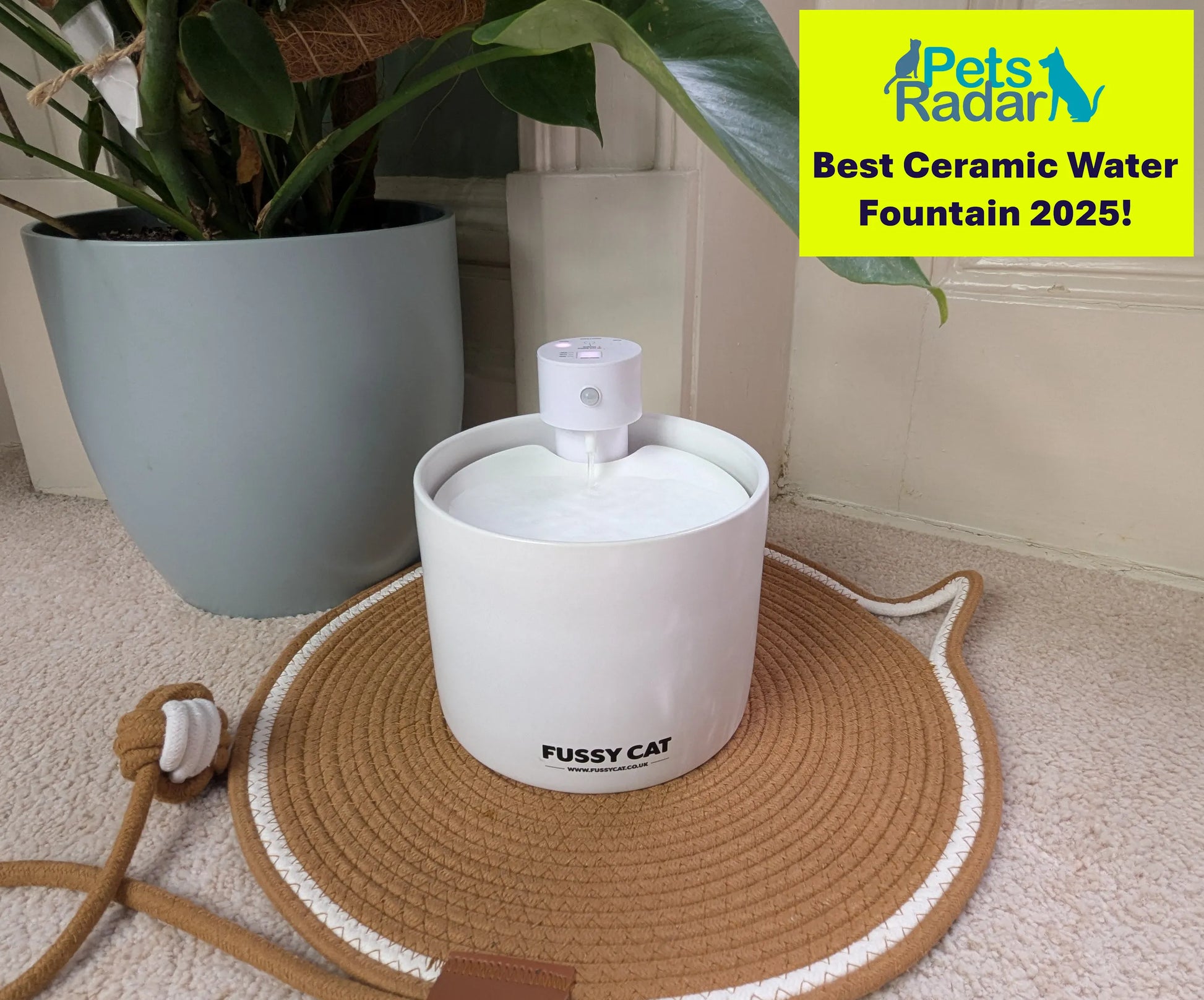 White ceramic Fussy Cat wireless water fountain with a pump, on a woven cat-shaped mat.