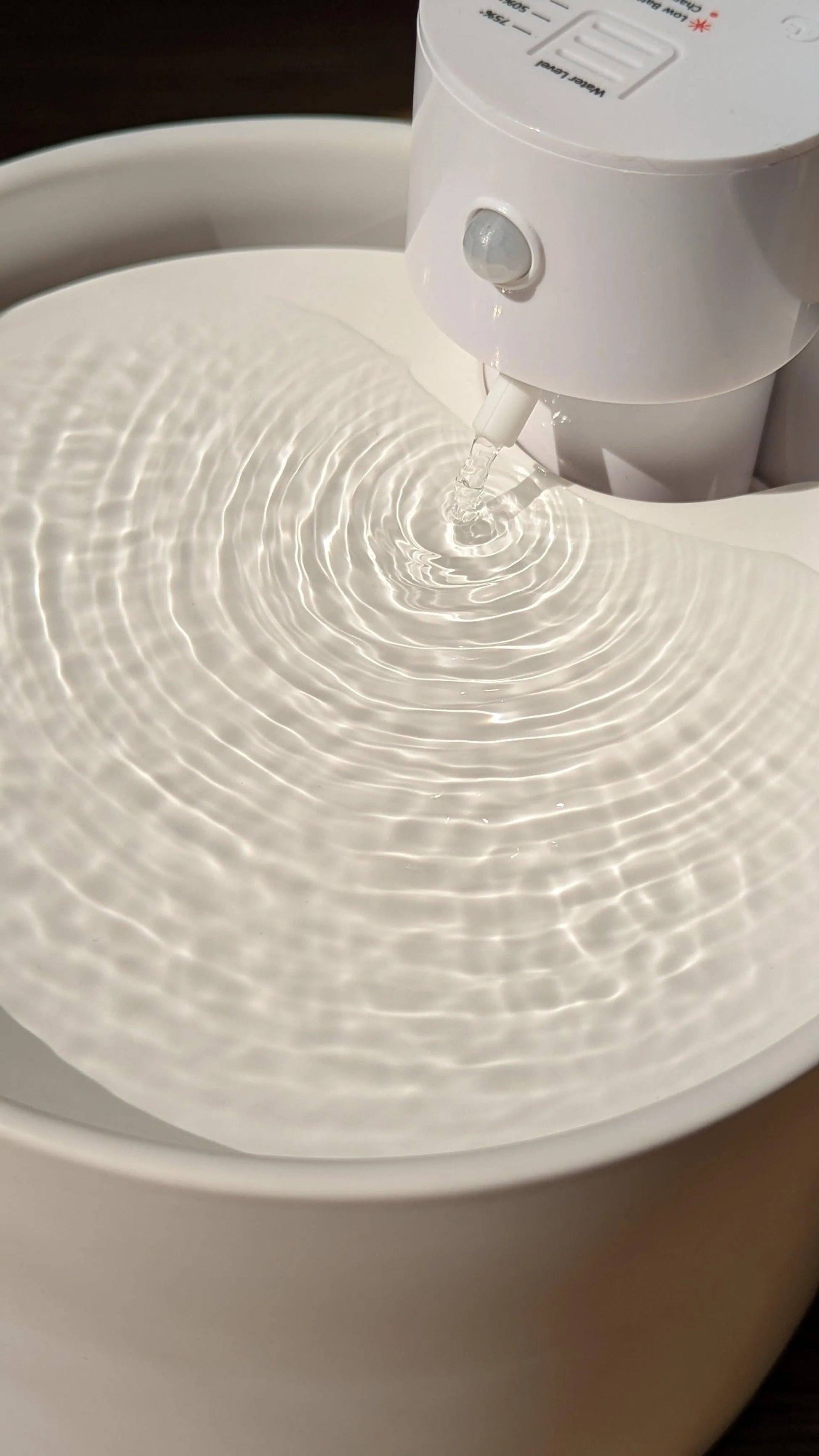 White ceramic cat water fountain with water rippling from a motion-sensor activated spout.