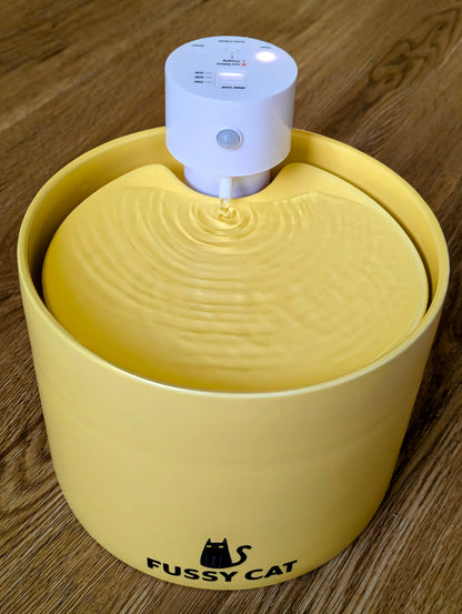 Yellow ceramic Fussy Cat water fountain with a white sensor unit and flowing water.