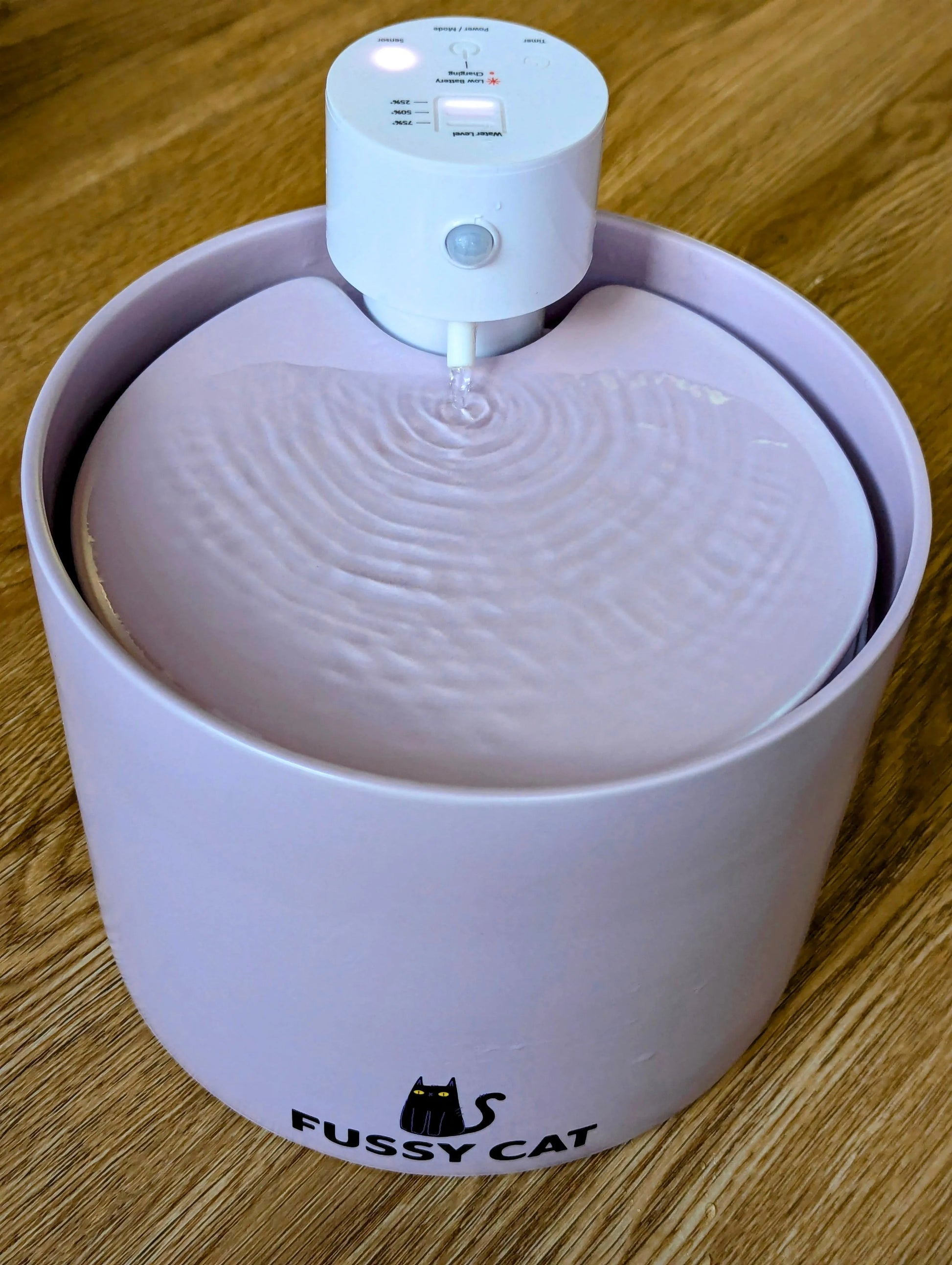 Fussy Cat wireless ceramic pet water fountain in lavender with a white motion sensor unit and flowing water.