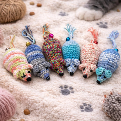 Six colorful, unique handmade crocheted wool catnip mouse toys on a cream textured blanket with paw prints.