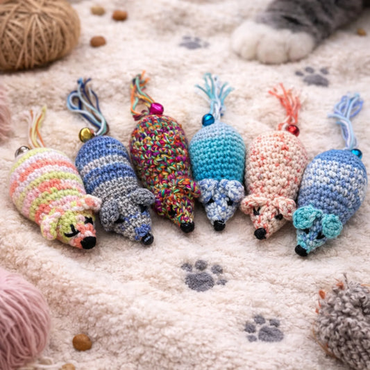 Six colorful, unique handmade crocheted wool catnip mouse toys on a cream textured blanket with paw prints.