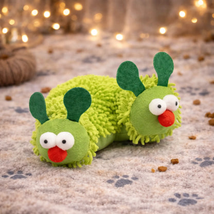 Soft plush green caterpillar cat toy with big eyes and red nose, on a paw print rug.