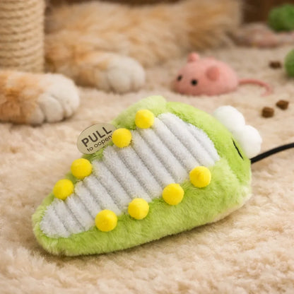 Green plush bug cat toy with yellow pom-poms and a "PULL to open" tag on a beige rug.