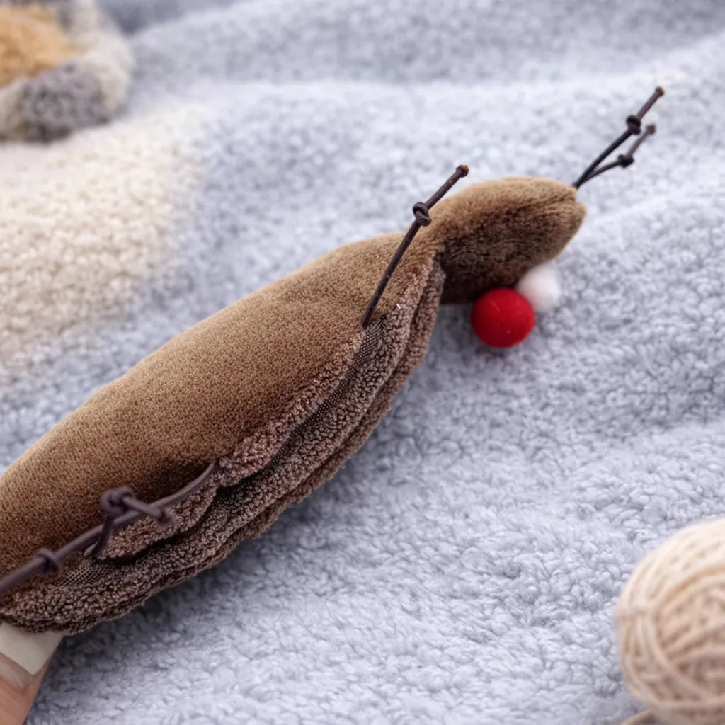 Brown plush cockroach cat toy with red nose and antennae on a soft grey blanket.