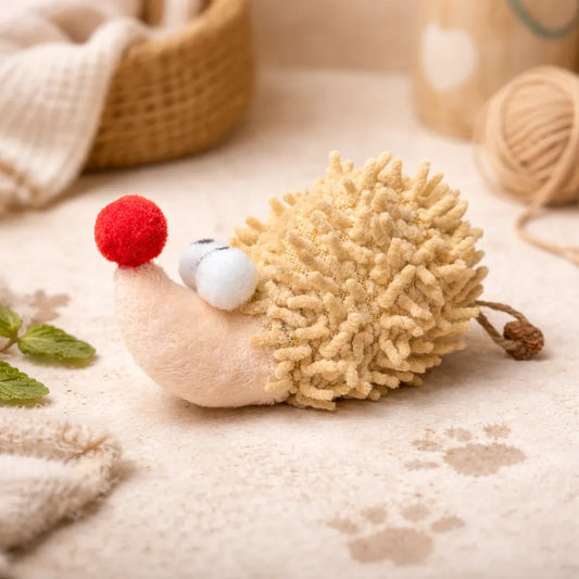 Beige plush hedgehog cat toy with fluffy back, red nose, and white eyes, on a light surface.